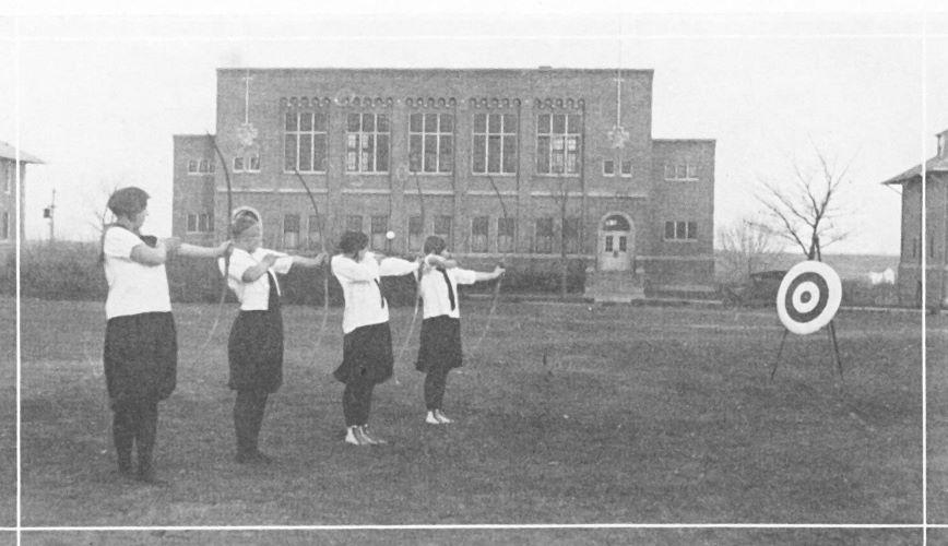 4 female students raise their bows to hit an archery target on the Campus Mall