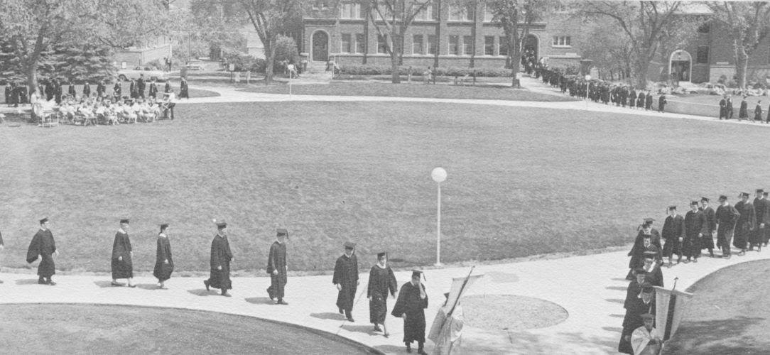 Graduates in their gowns process to commencement on the Campus Mall