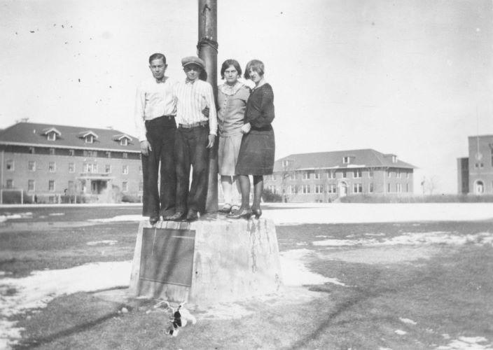 4 students stand on the flagpole base for the WWI memorial on the Campus Mall