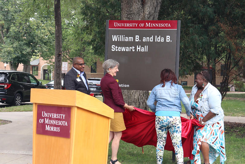 Four people take the red cloth cover off the new William B. and Ida B. Stewart Hall sign