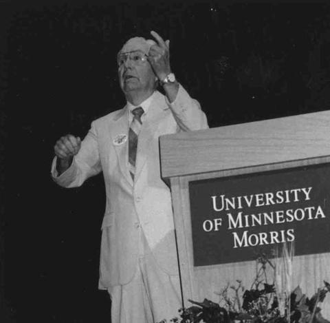 Image of Ralph Williams by a podium with a plaque saying University of Minnesota Morris